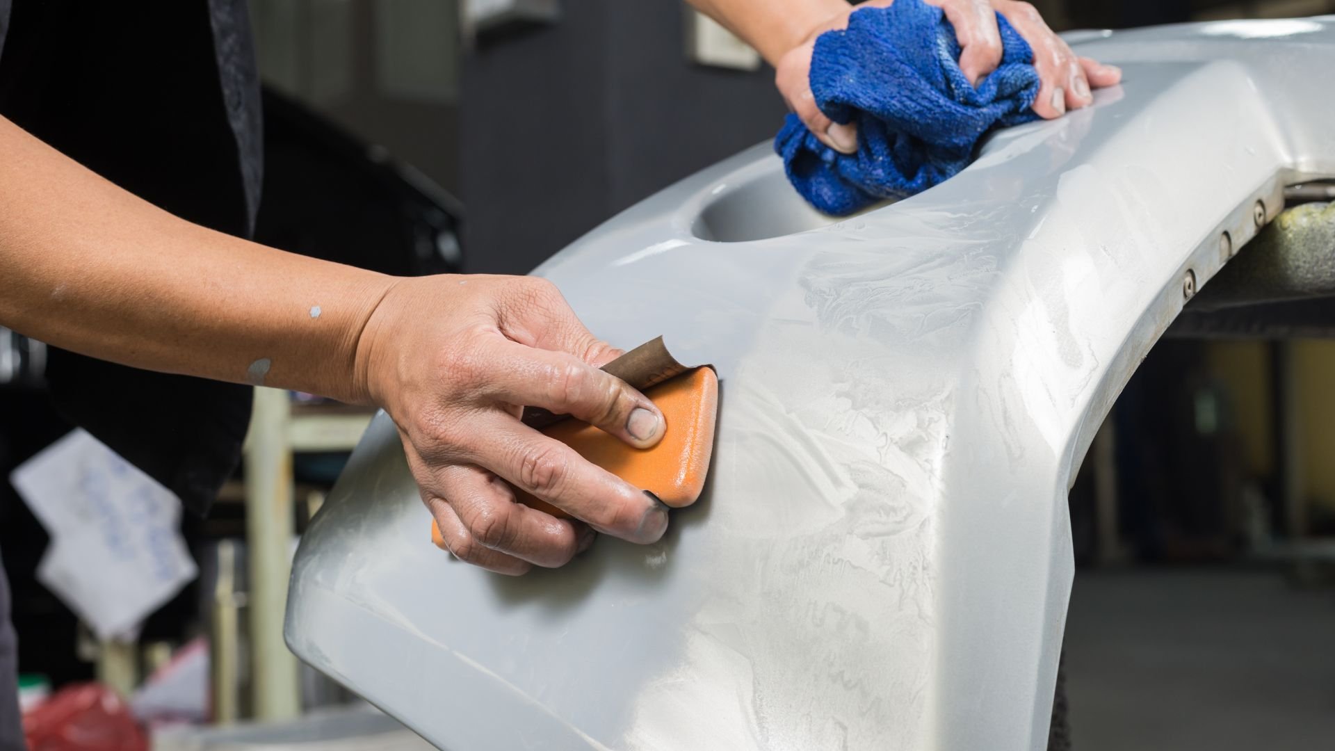 Hand sanding car body panel with orange sanding block and blue towel
