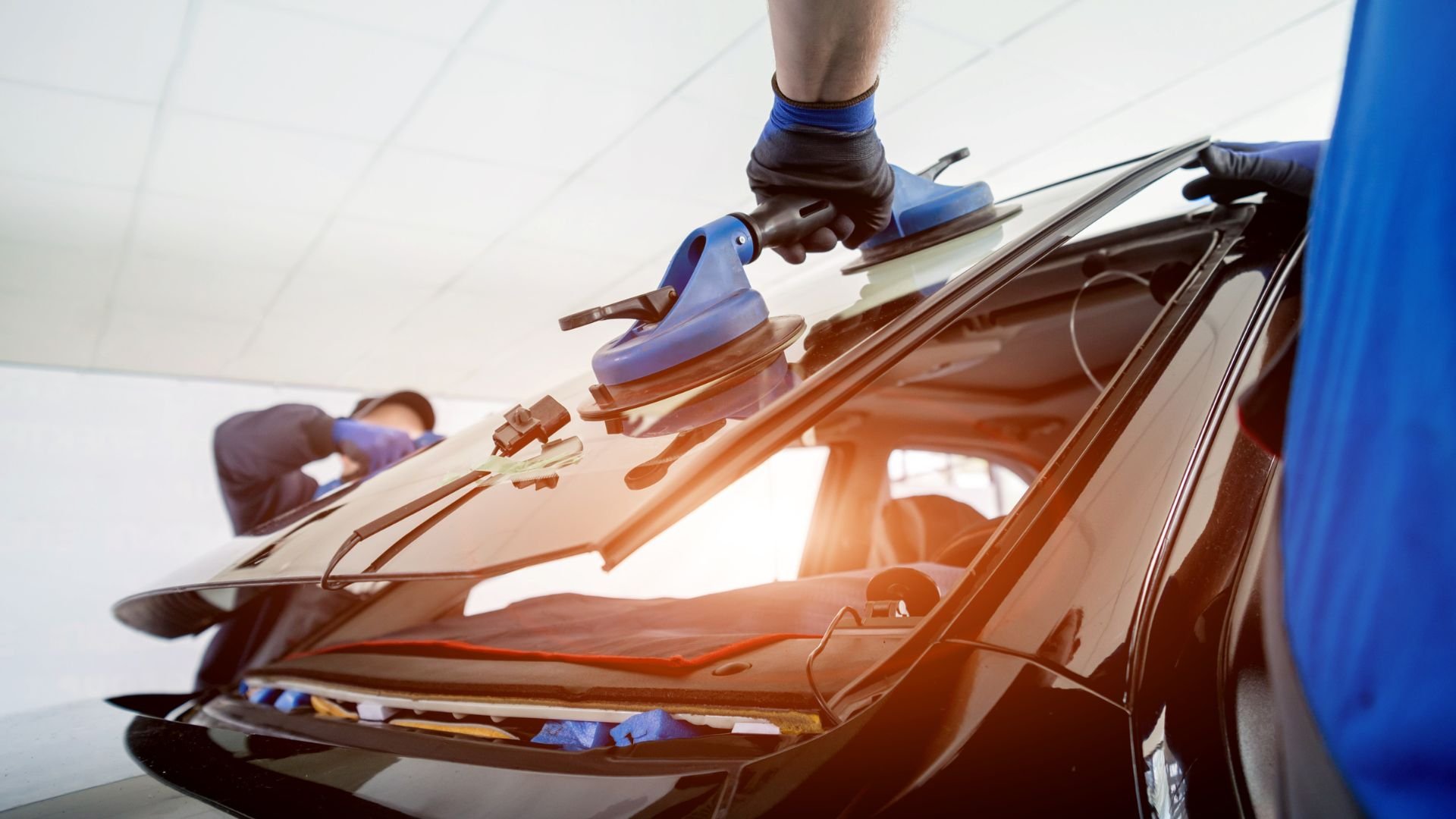 Technician replacing car windshield with professional tools and gloves
