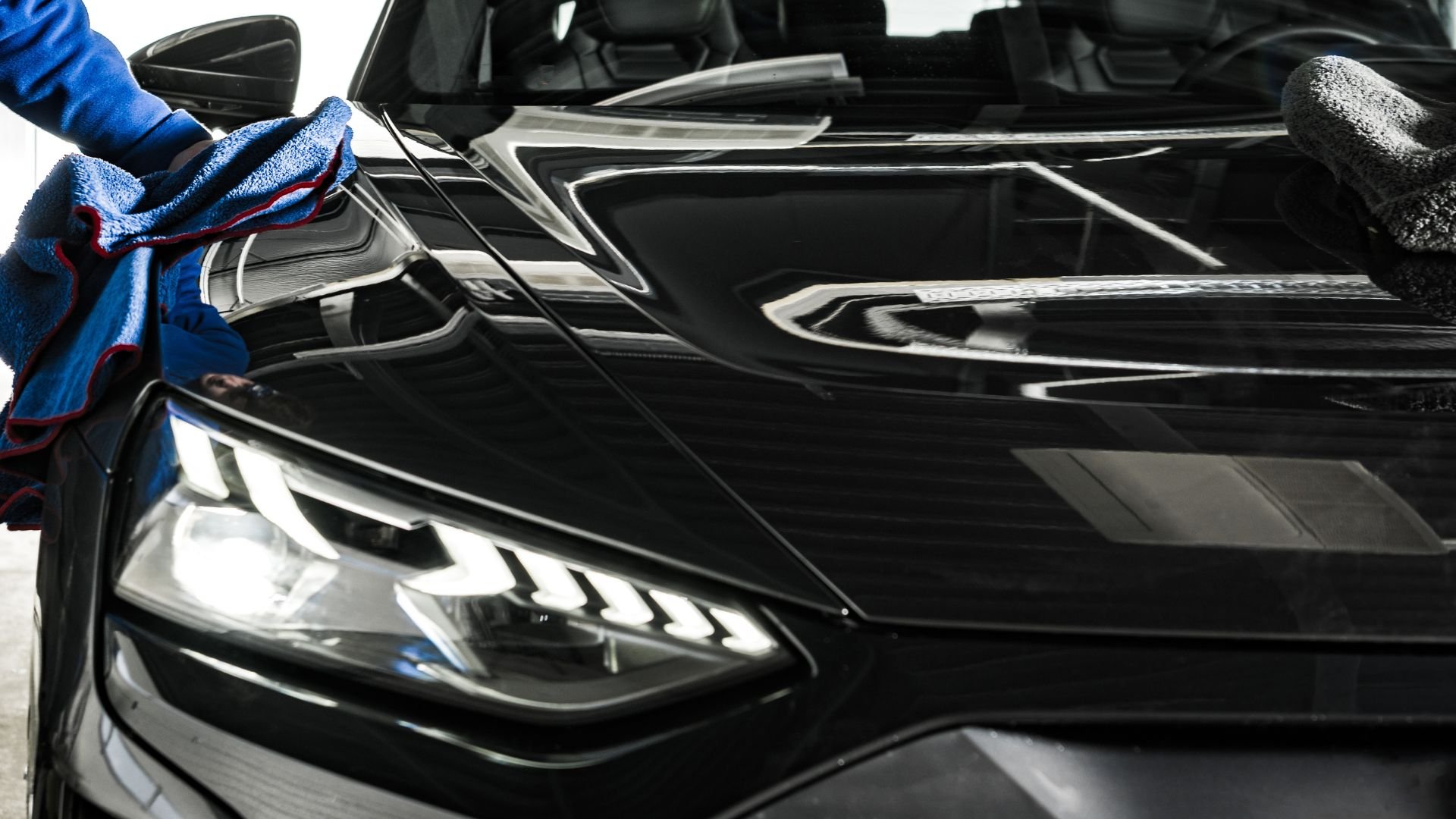 Blue microfiber towel cleaning sleek black car headlight and body
