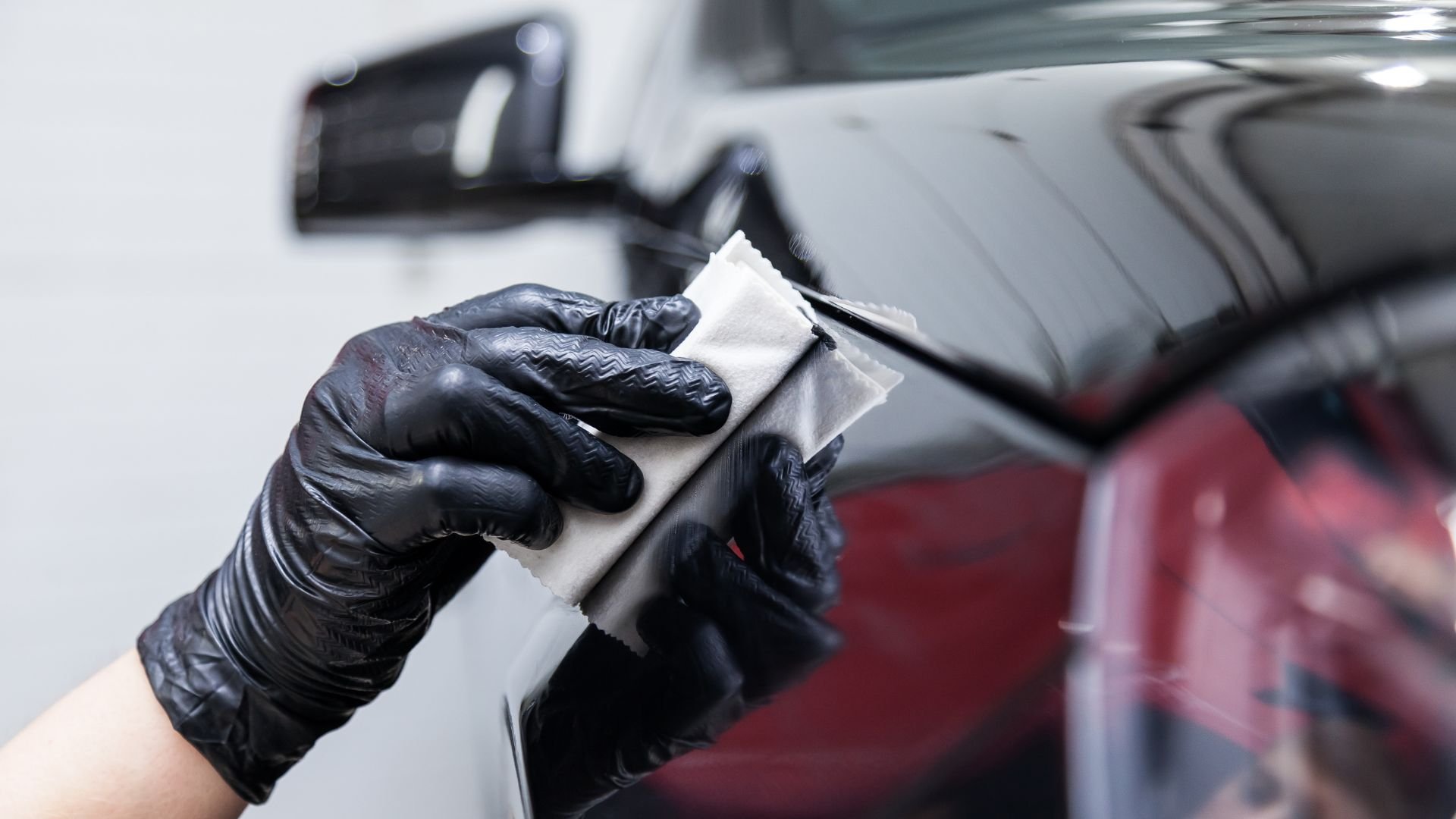 Gloved hand polishing a shiny car surface with a white cloth