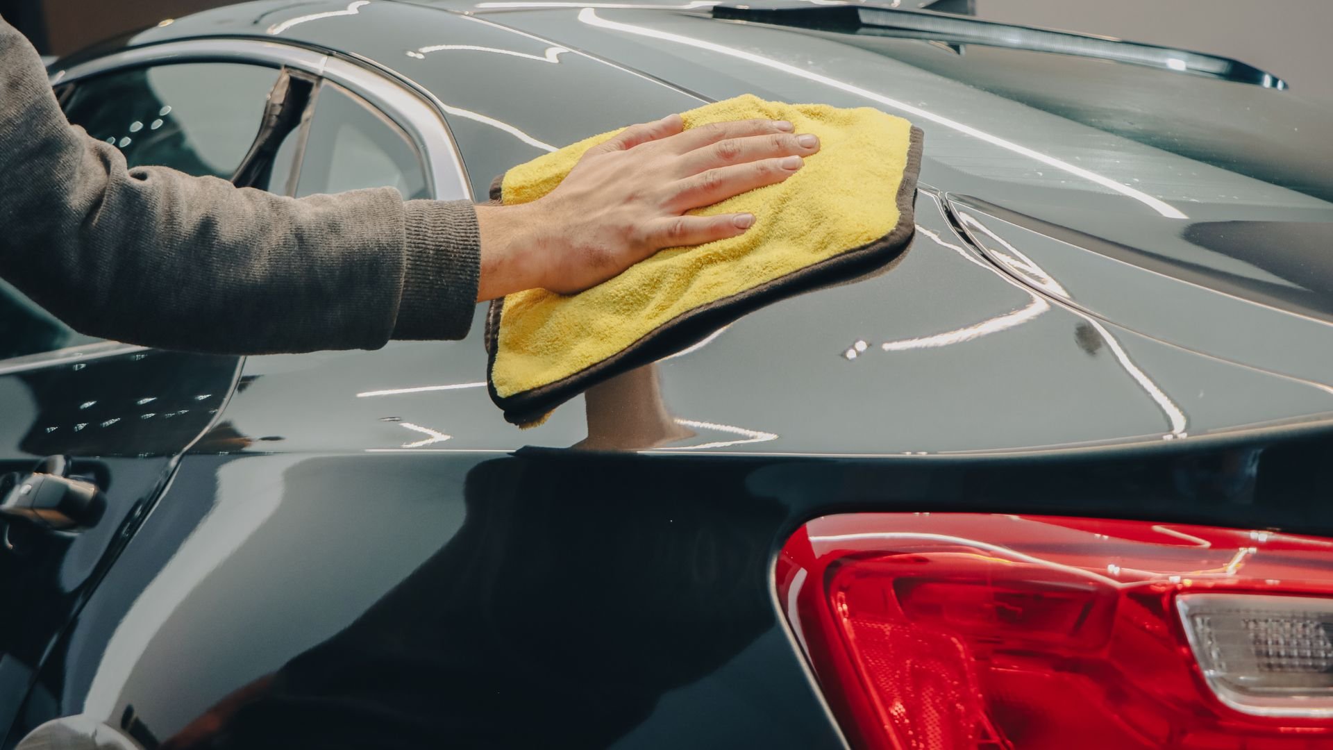 Hand wiping gray car with yellow microfiber cloth
