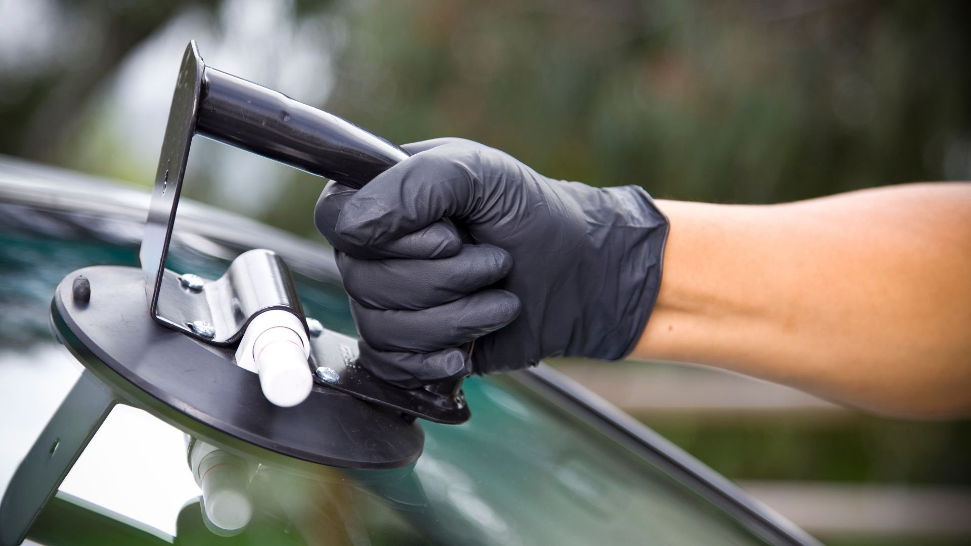 Gloved hand using tool to repair or replace car windshield glass