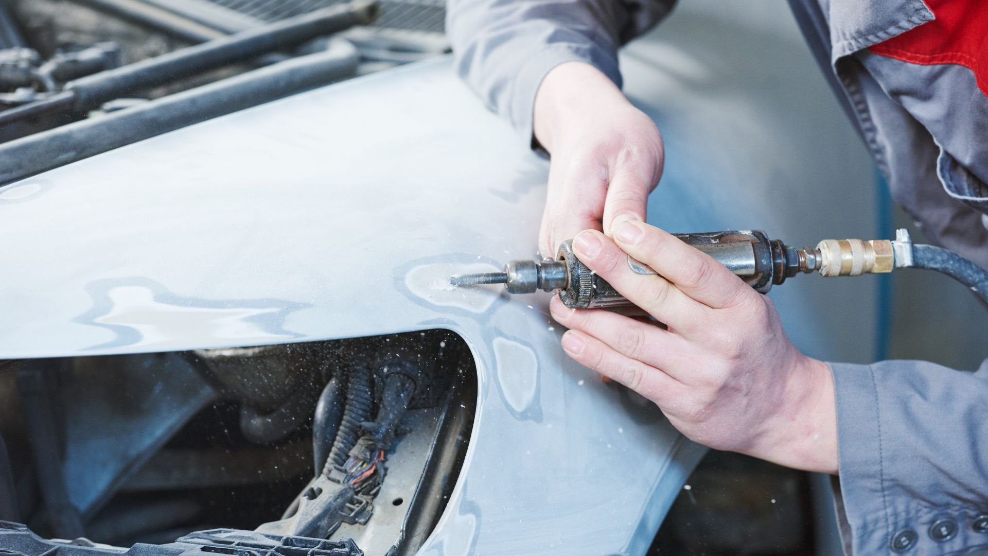 Mechanic using pneumatic drill to repair car body panel