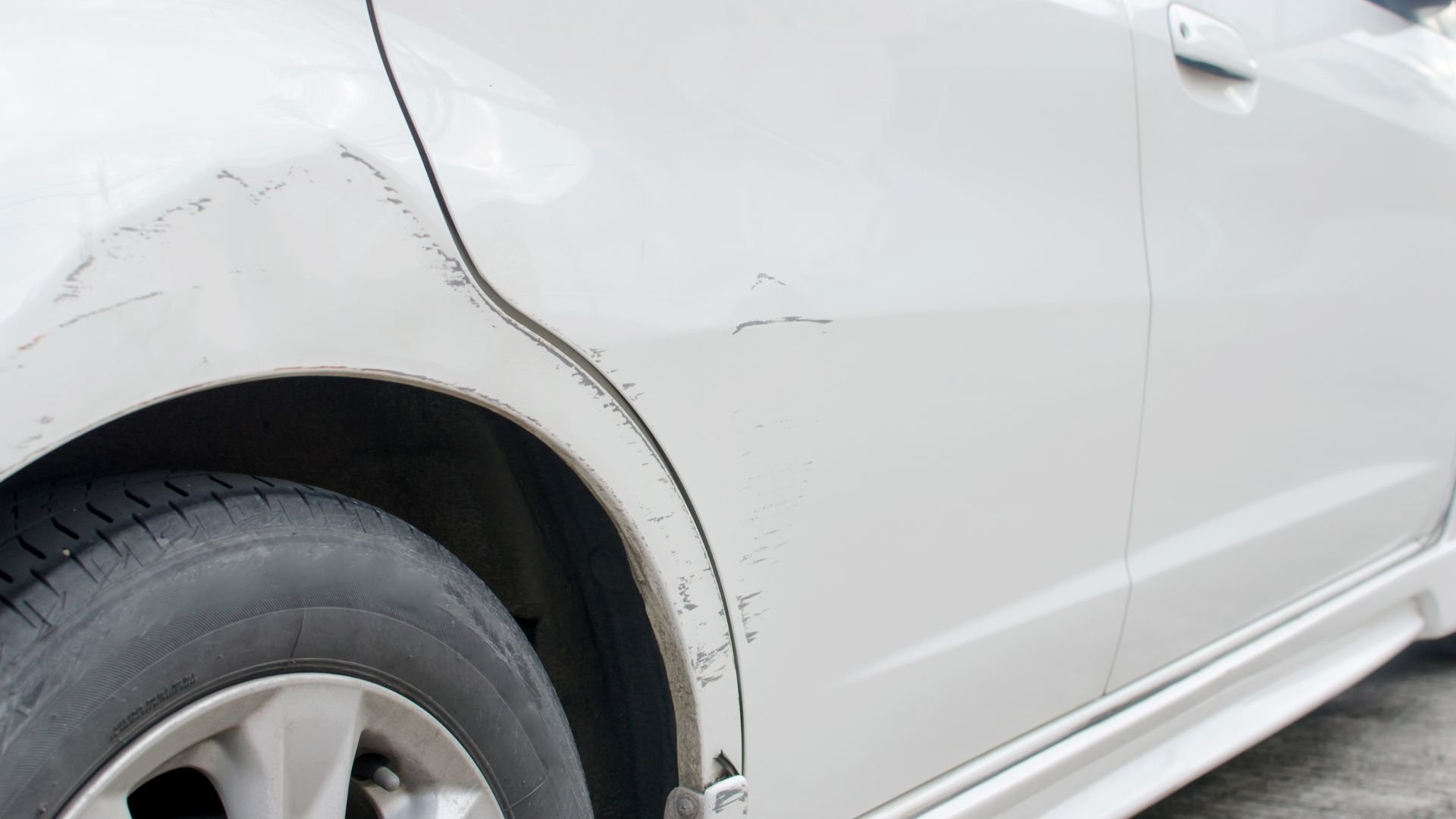 White car with scratched and damaged side panel near wheel