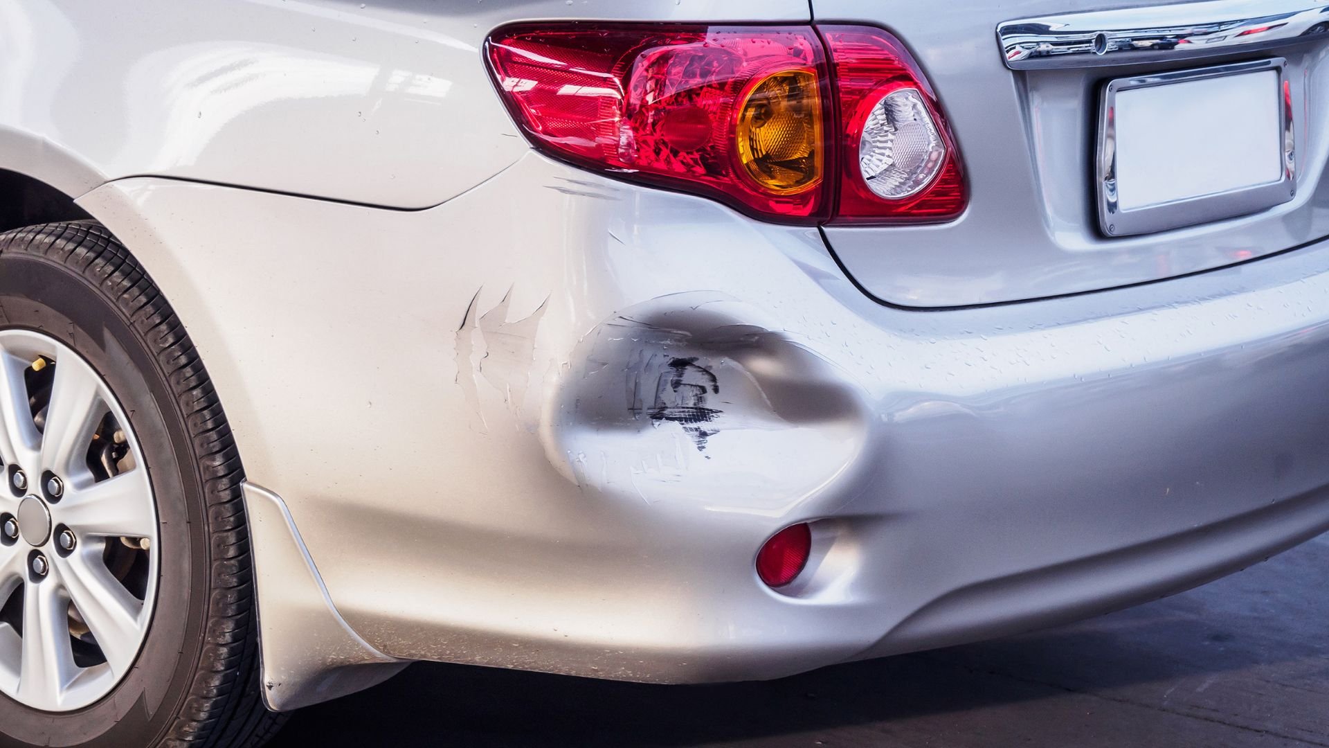 Silver car with dented bumper and visible damage near rear taillight