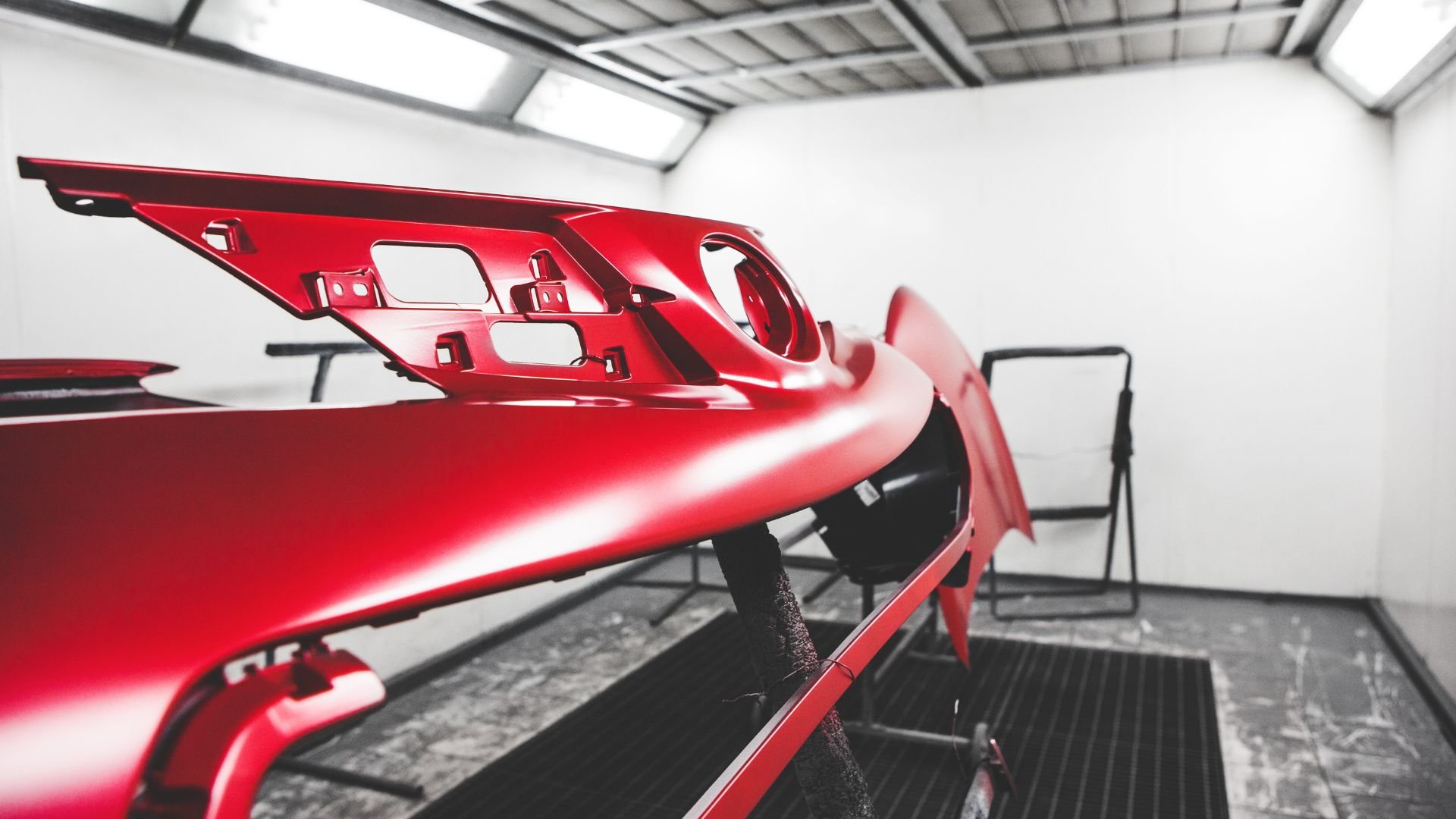 Glossy red car body panel in automotive paint shop workshop