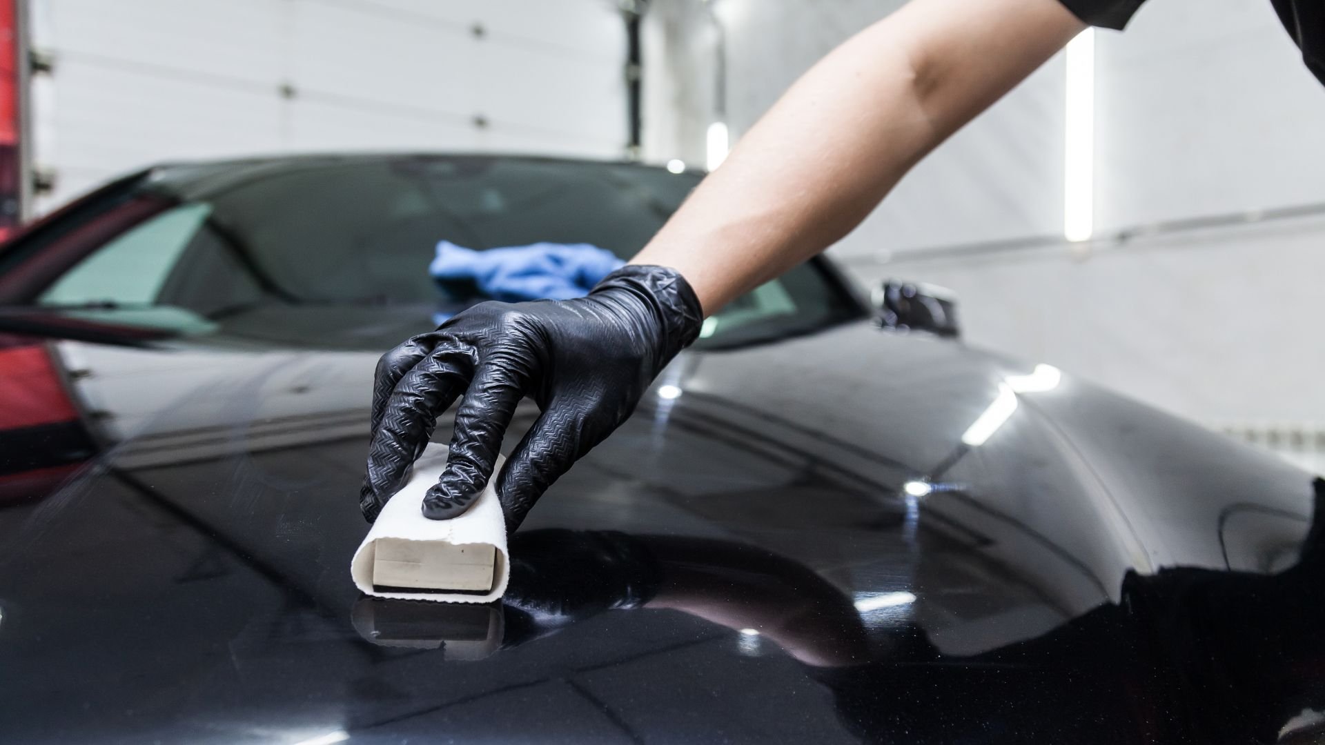 Worker in gloves polishing a sleek black car surface