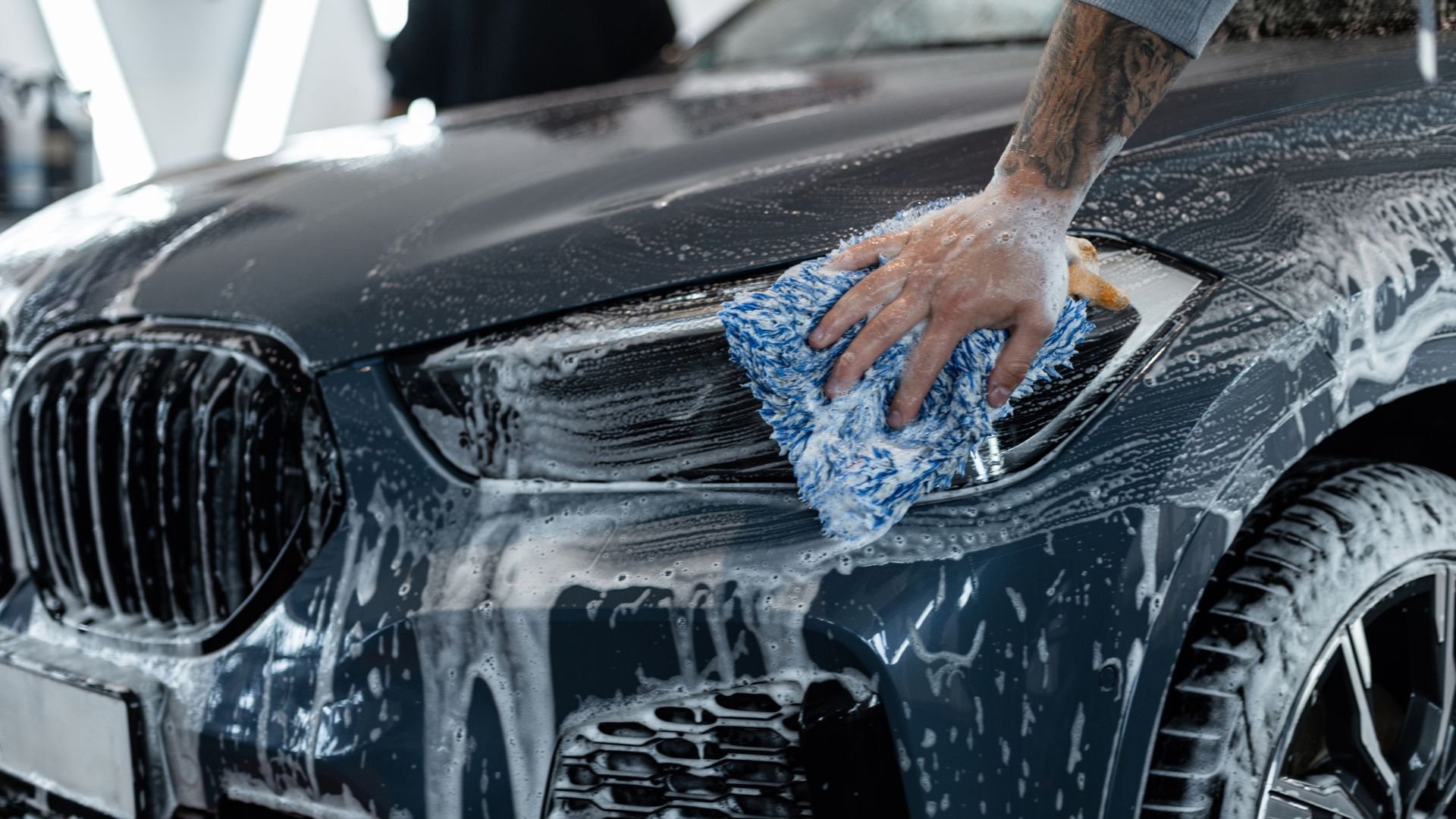Hand washing black BMW with blue and white microfiber cloth