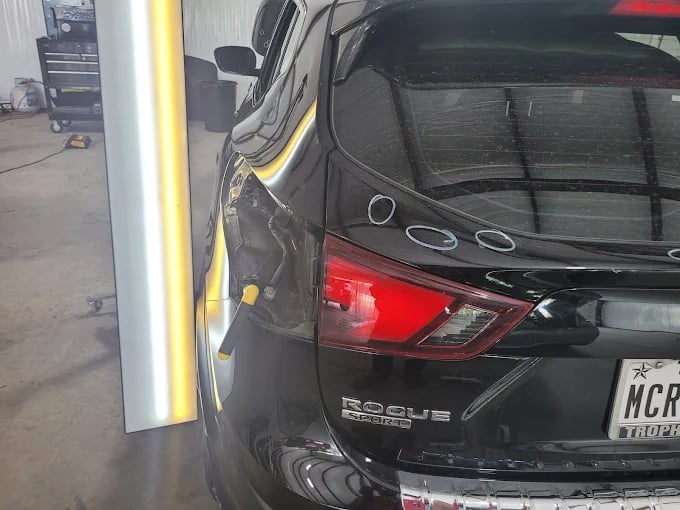 Black Nissan Rogue with red taillight in auto repair shop
