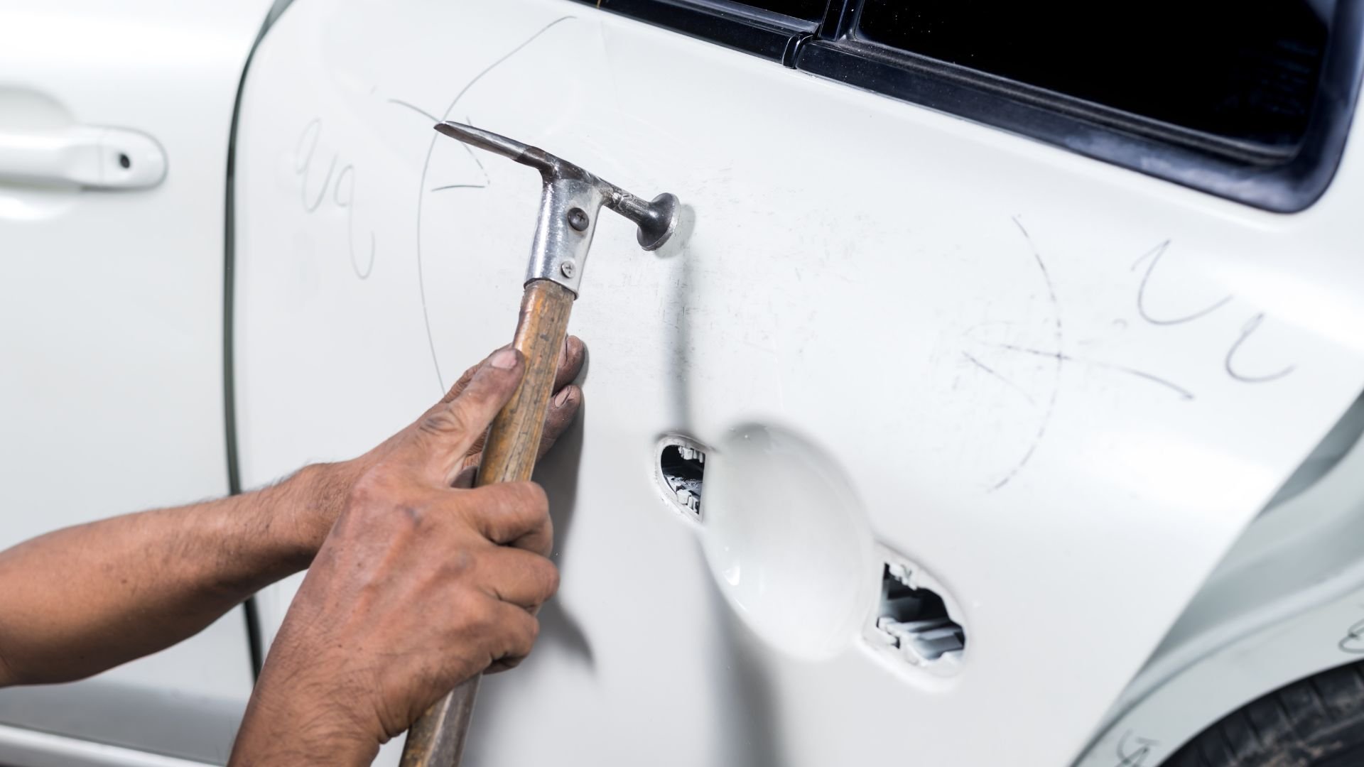 Hand using hammer to repair dent on white car body