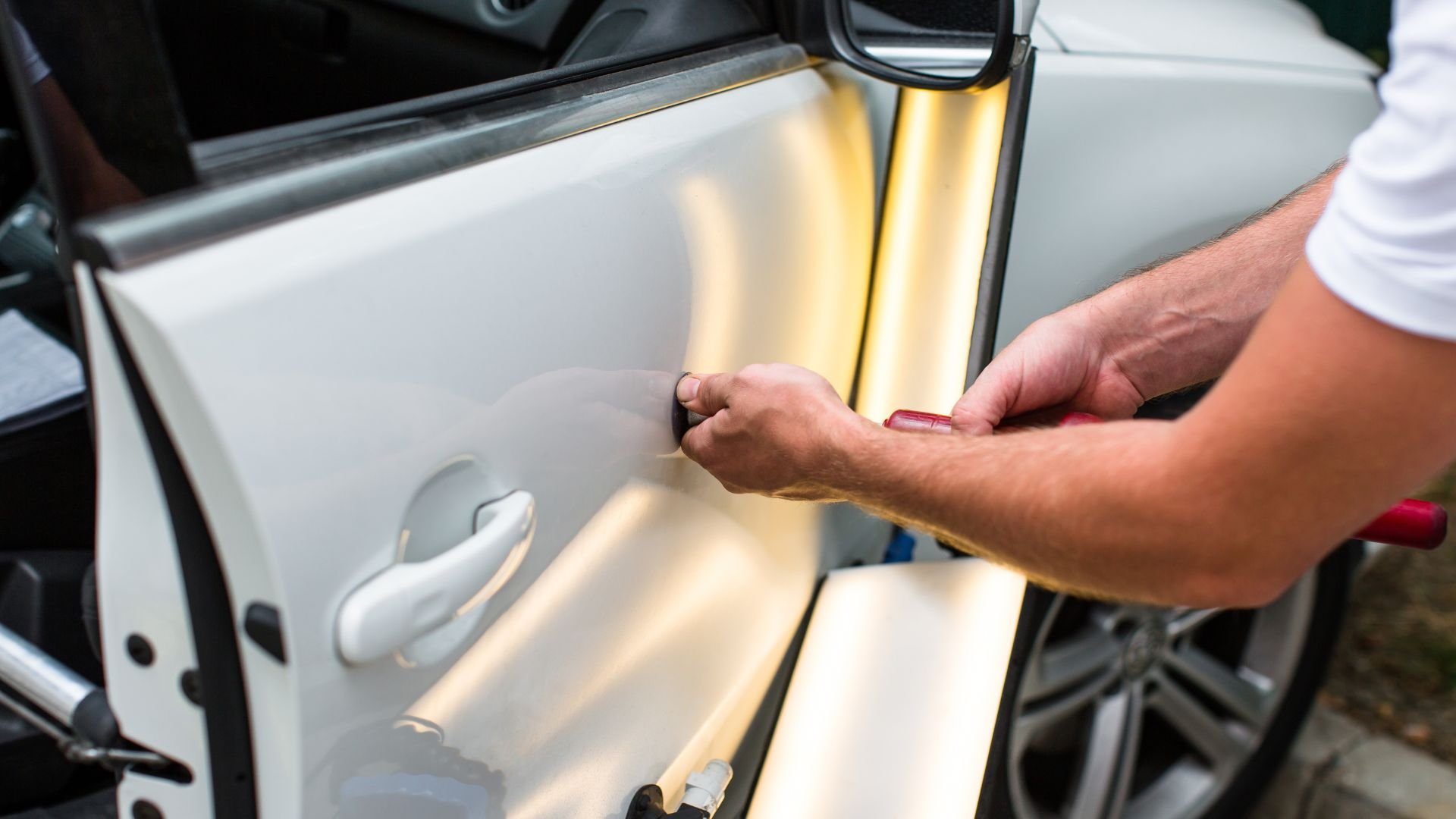 Hand opening car door with warm light reflecting on white vehicle
