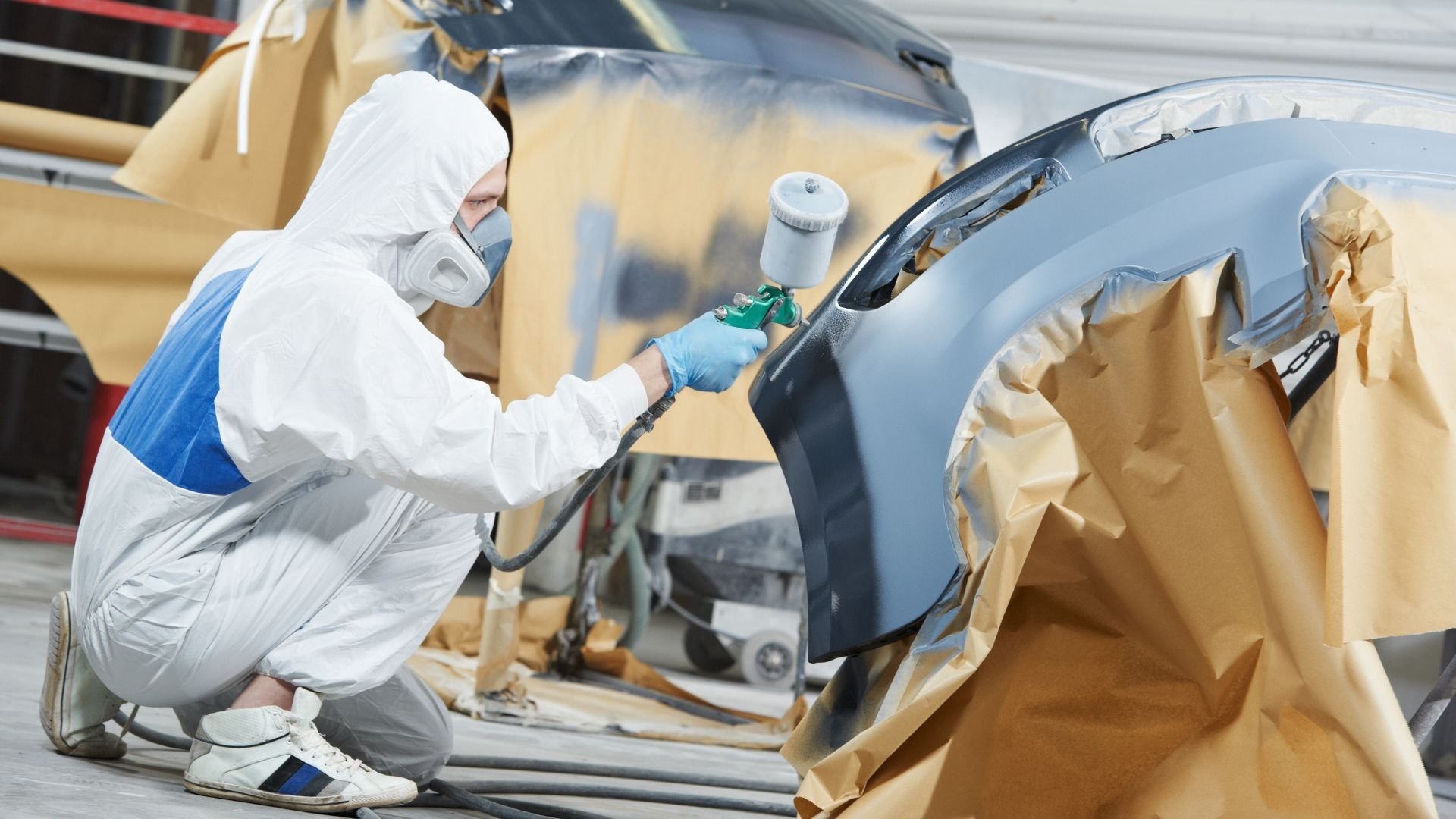 Auto body worker in protective suit spray painting a car panel